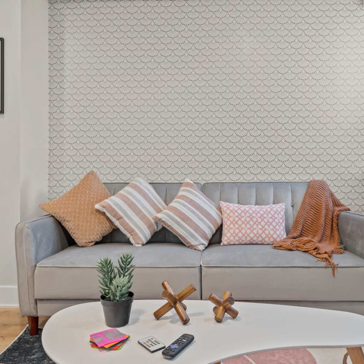 A modern living room with a gray sofa adorned with various colored pillows, a small table with decorative items, and a patterned wall in the background.