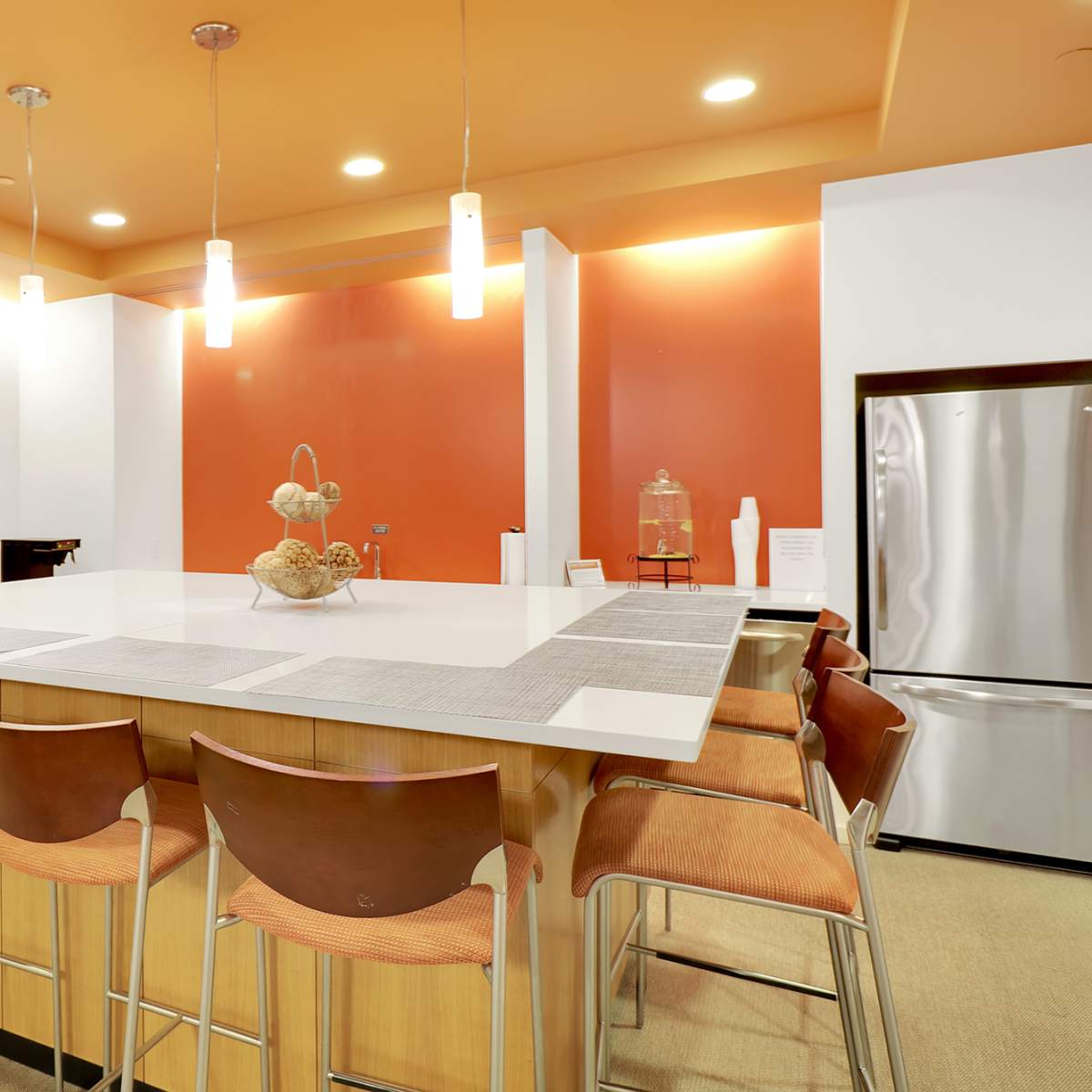 The kitchen features a large island with barstools, wooden cabinetry, and an orange accent wall.