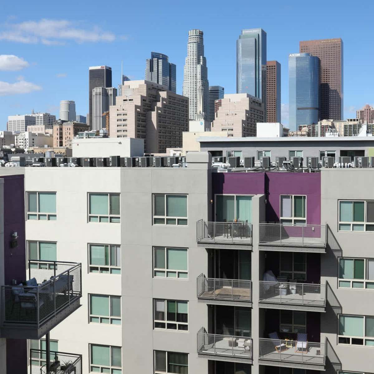 A view of modern apartment buildings with balconies in the foreground and a skyline of high-rise buildings in downtown Los Angeles in the background.