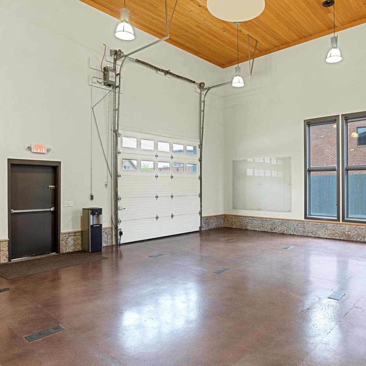 A spacious, empty interior room with large windows, a high ceiling, and a garage door on one wall.