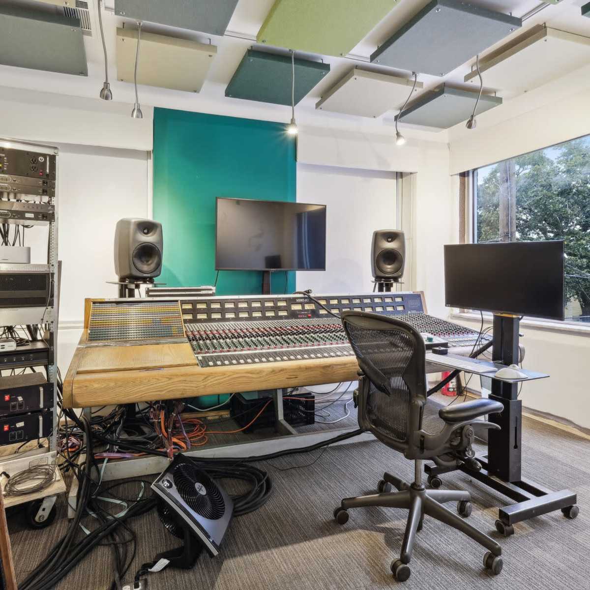 A recording studio features a large audio mixing console surrounded by sound equipment and monitors.