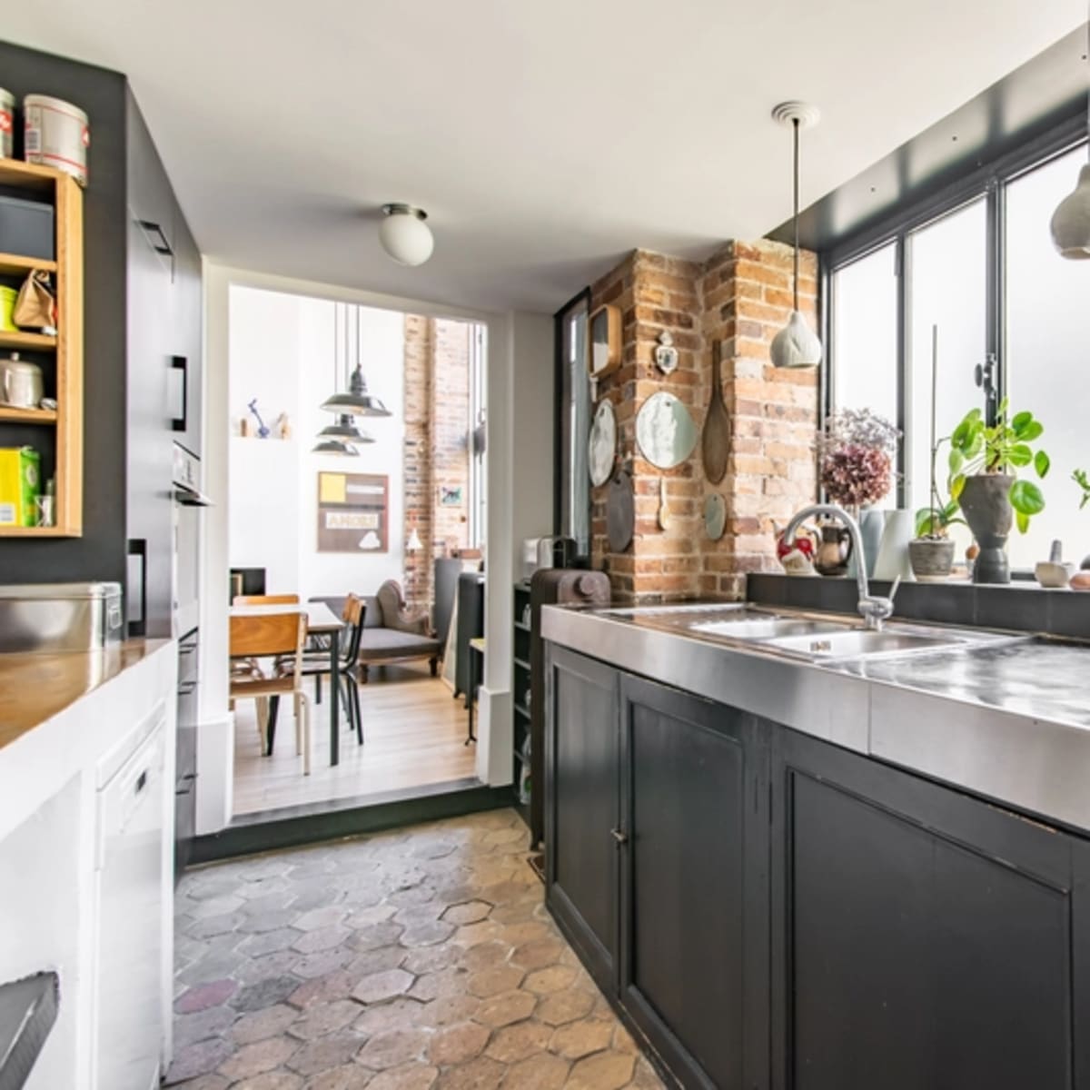 A modern kitchen with a black cabinetry, a stainless steel countertop, and large windows allowing natural light to enter.