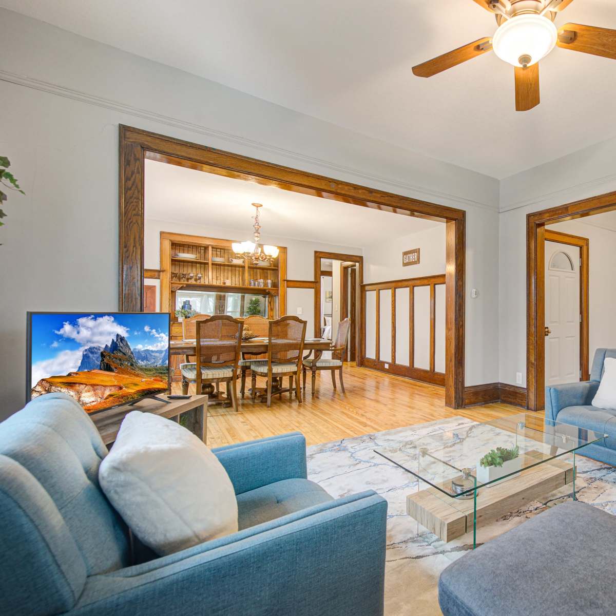 A spacious living area features a ceiling fan, a glass coffee table, comfortable seating, and an open layout leading to a dining space.