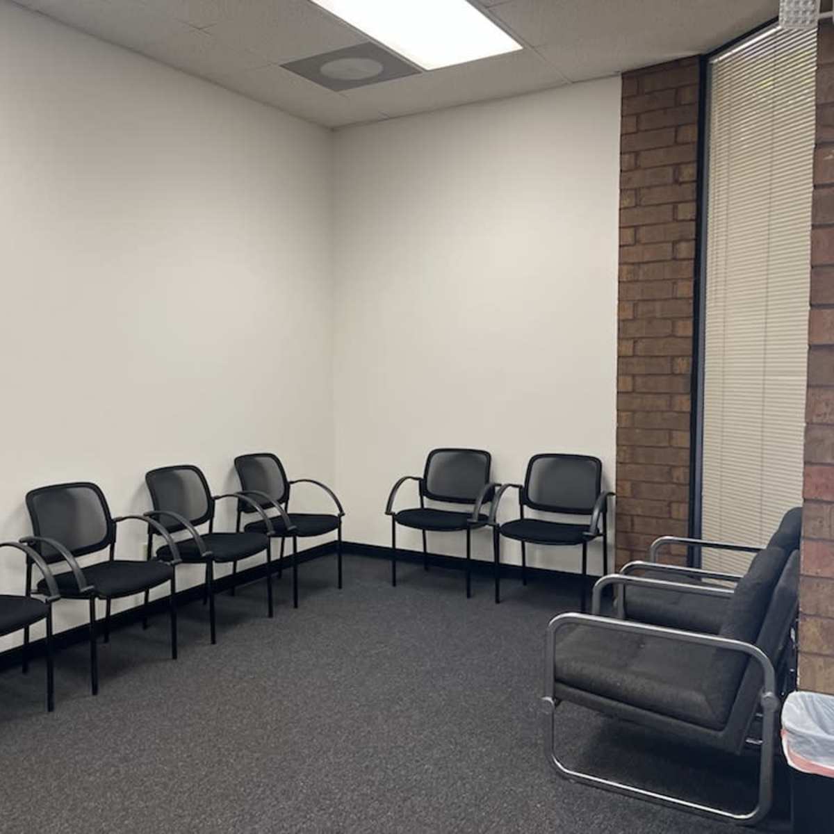 A waiting room with several black chairs arranged against a plain white wall.