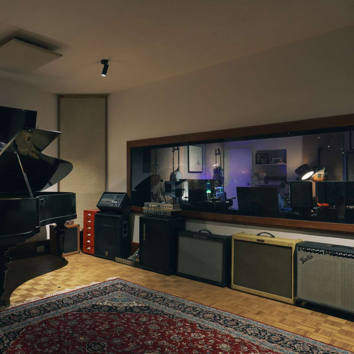 A music studio with a grand piano, recording equipment, and a plush rug on a wooden floor.