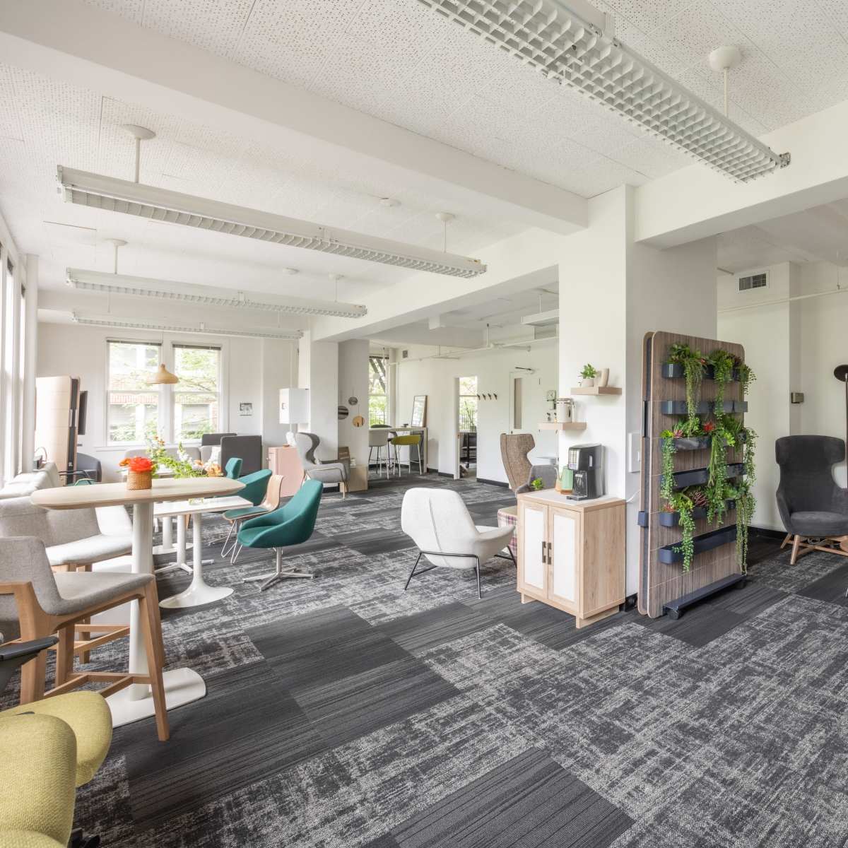 A spacious, modern open area with various seating options, a bookshelf with plants, and large windows allowing natural light.