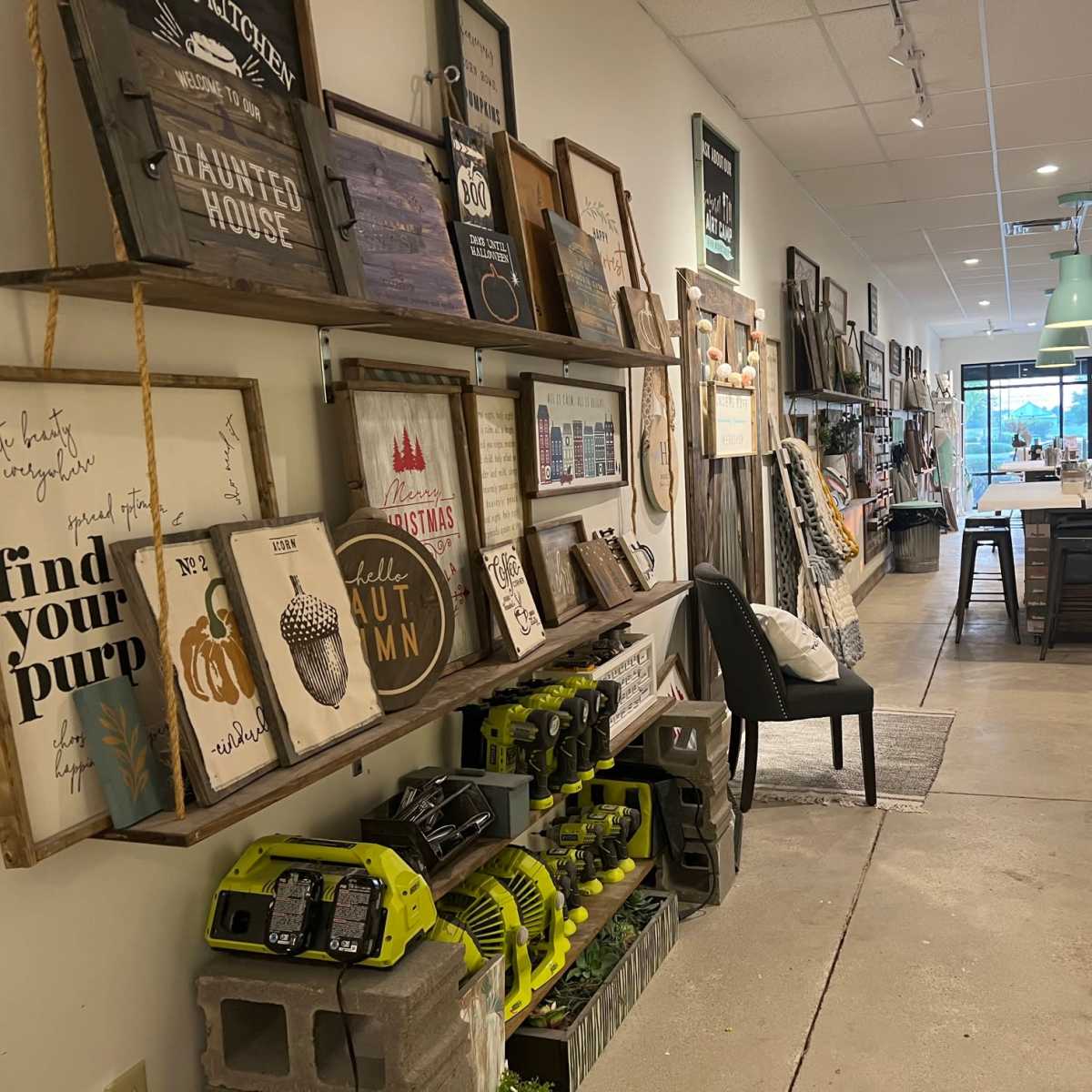 The interior of a retail store with shelves displaying various signs and home decor items, alongside a row of tools and a seating area.