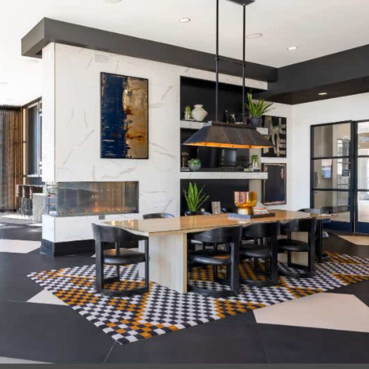 A modern dining space featuring a large table, black chairs, a patterned rug, and a marble fireplace with art on the walls.