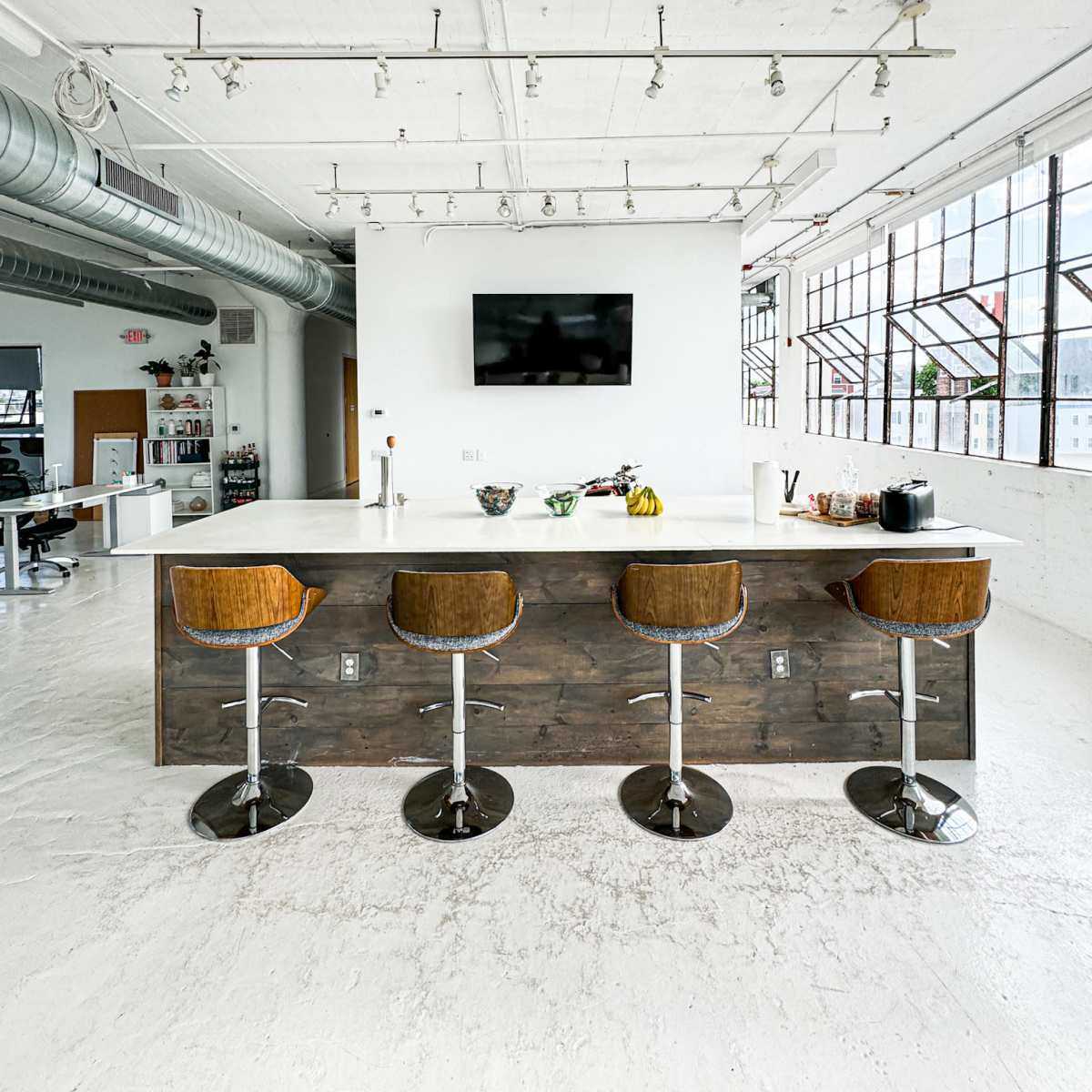 A modern kitchen features a large island with four wooden bar stools and a wall-mounted television above.