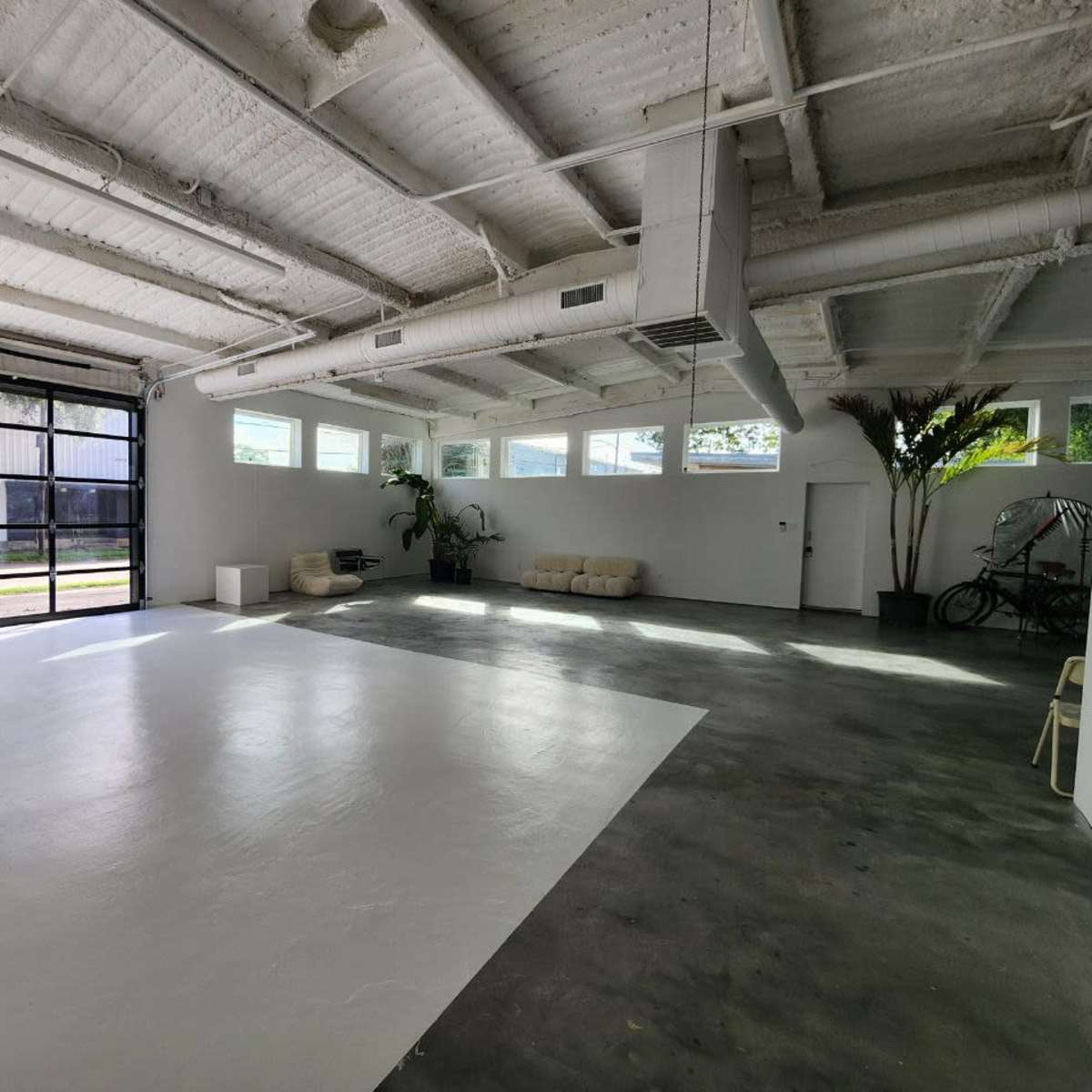 A spacious garage with a polished white floor, large glass doors, and minimal furnishings including a sofa and potted plants.