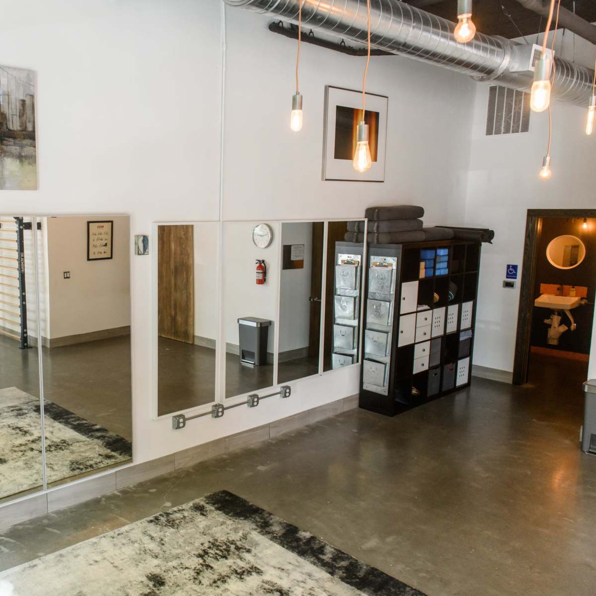 The interior of a modern, well-lit space features large mirrors, a rug, and storage units, with artwork displayed on the walls.