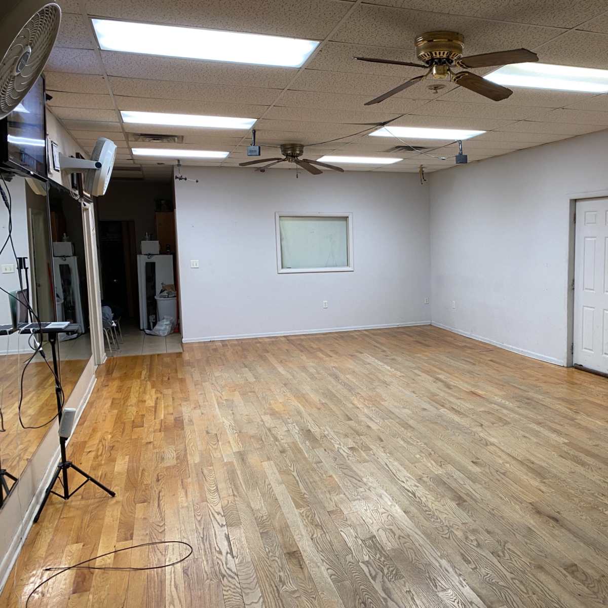 An empty room with hardwood floors, a door, a wall mirror, a camera on a tripod, and ceiling fans.