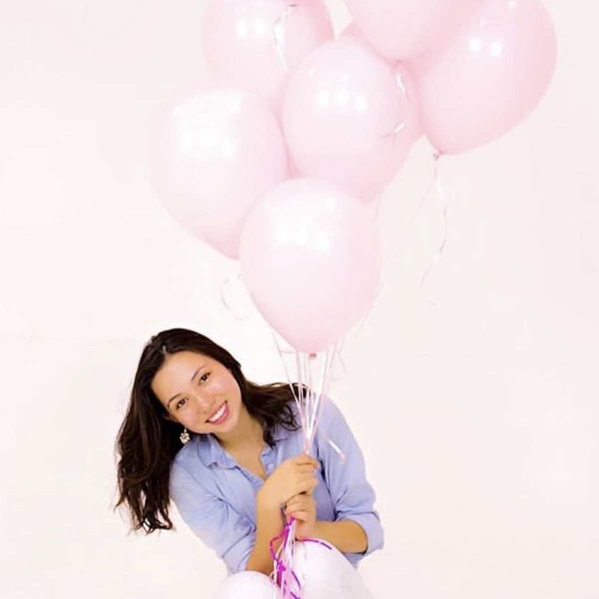 A person kneels while holding a bouquet of pink balloons against a white background.