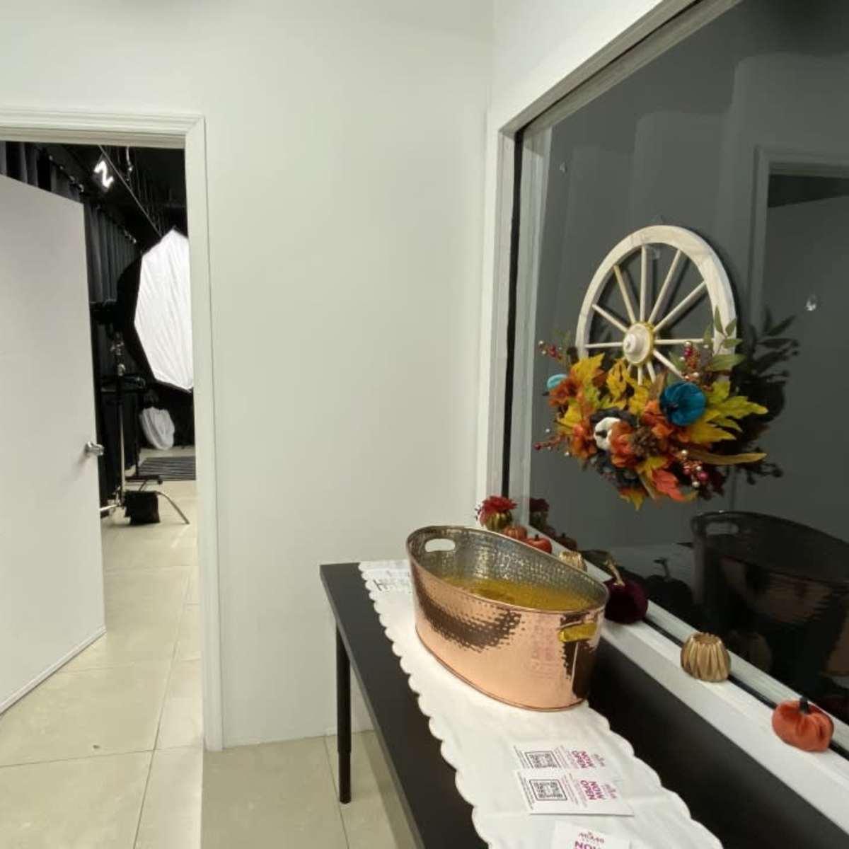 A hallway with a doorway leading to another room, featuring a table with a decorative bowl and a seasonal floral arrangement on a wall-mounted mirror.
