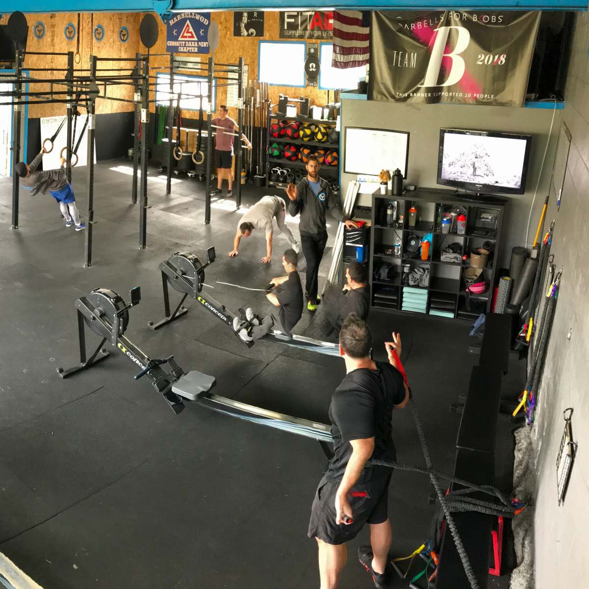 A gym interior with multiple exercise stations, including rowing machines and weightlifting equipment, where several people are engaged in various workouts.