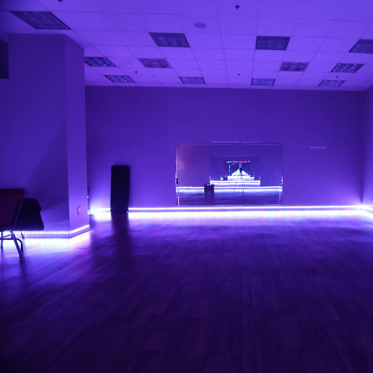 A spacious room features purple walls and LED lighting along the floor, with a large mirror reflecting the light.
