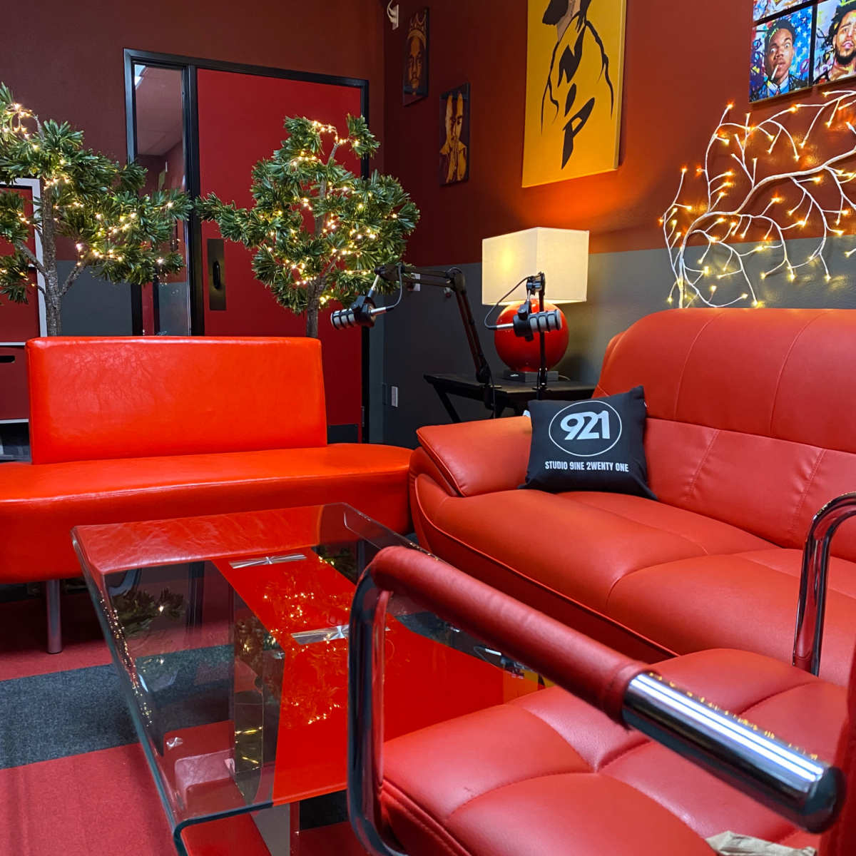 A modern lounge area with red furniture, a glass coffee table, and festive decorations, including wreaths and string lights.