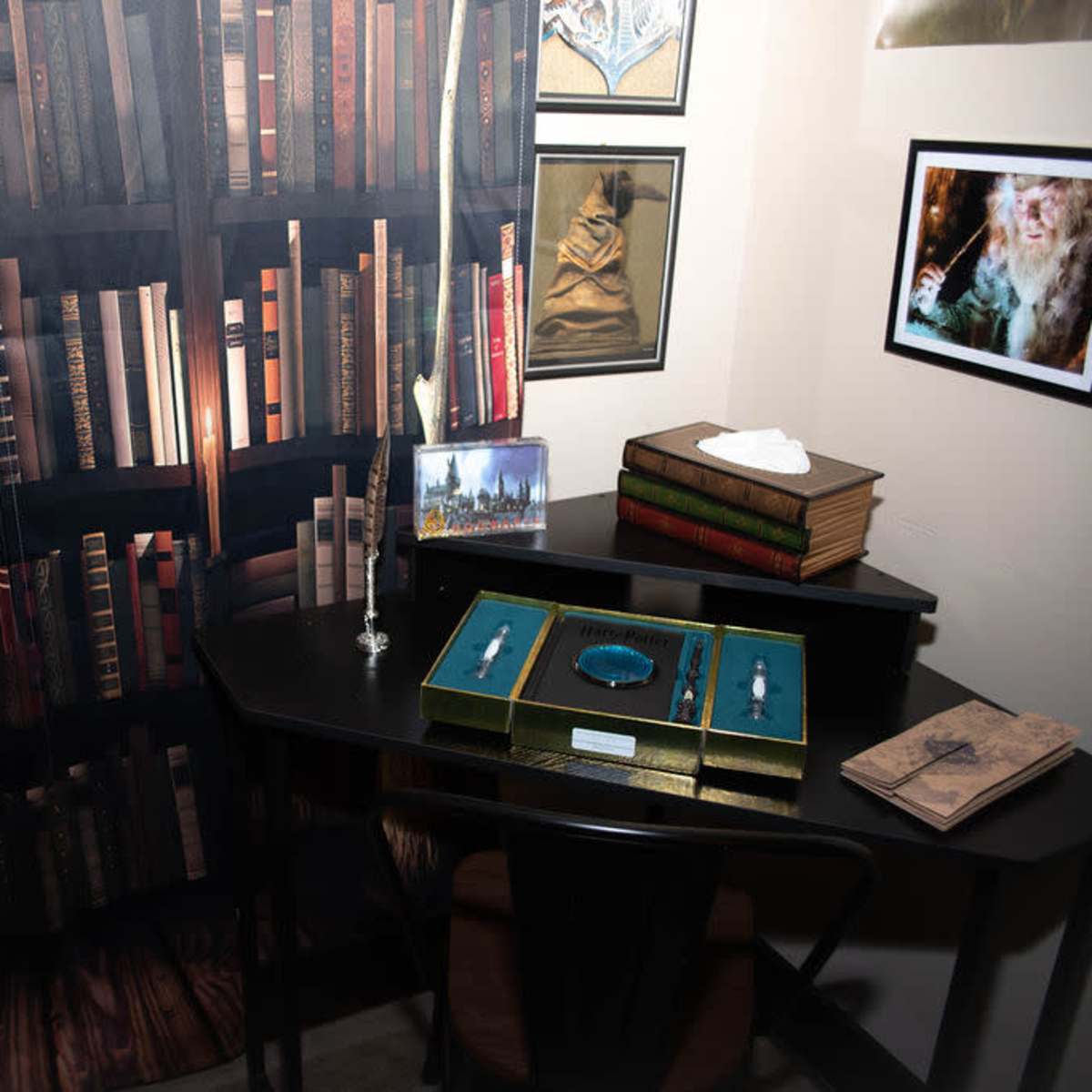 A small desk with a display of jewelry boxes and books, set against a backdrop of a bookshelf filled with various books and a few framed pictures on the wall.