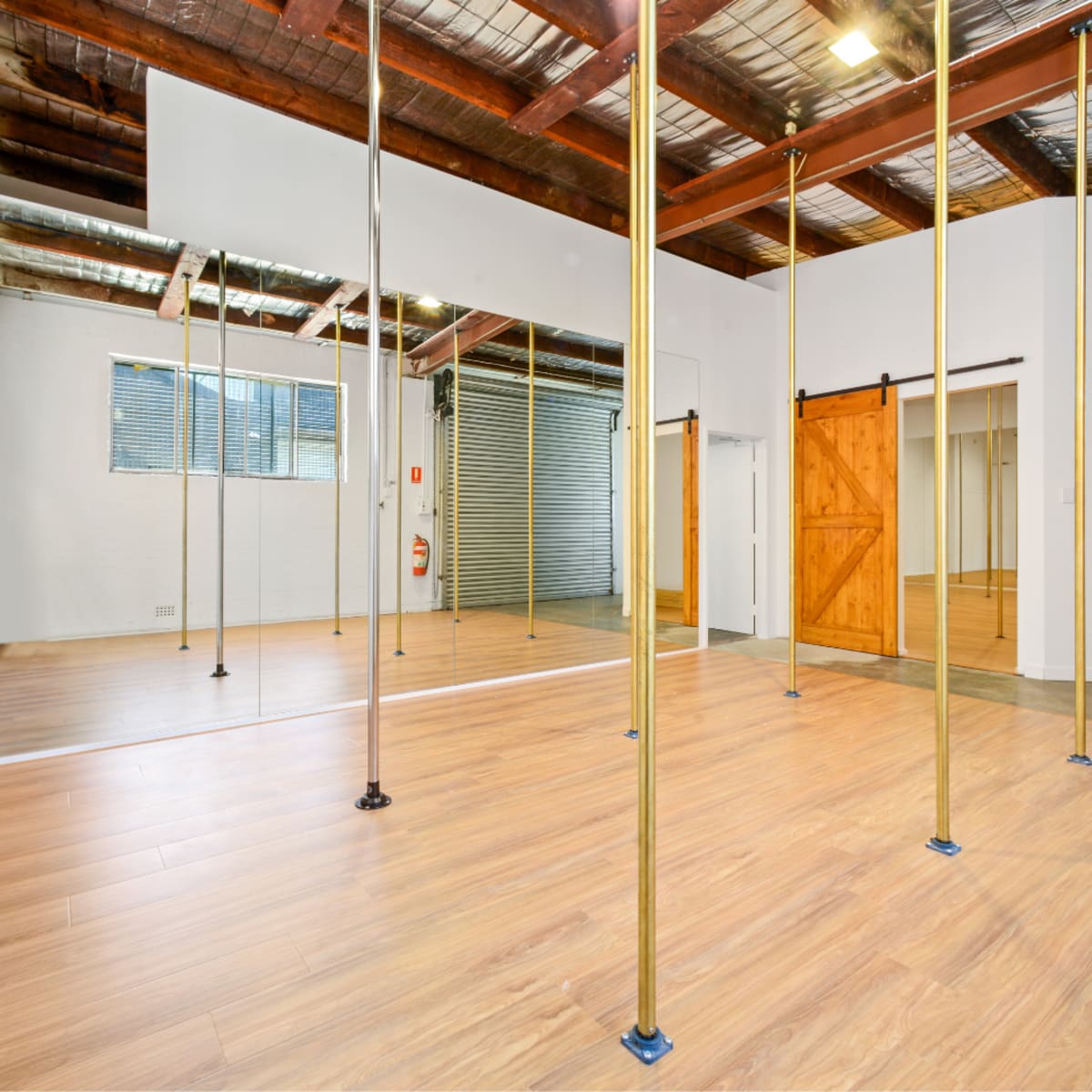 An open studio space with wooden floors, gold poles, mirrors, and sliding barn doors.