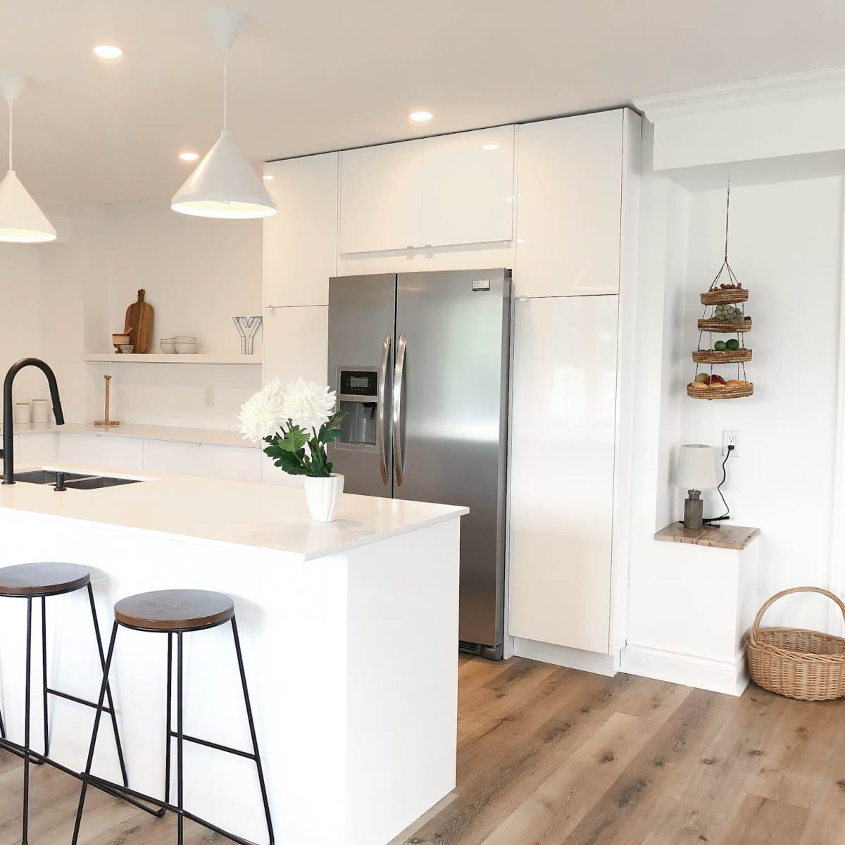 A modern kitchen featuring a central island with three stools, stainless steel appliances, and white cabinetry.