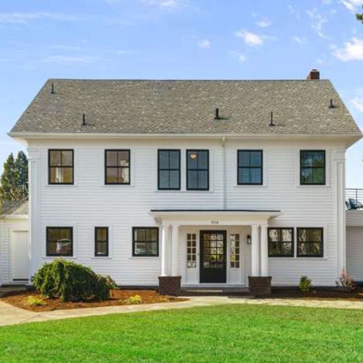 A two-story white house with black trim, a central entrance, and a landscaped front yard.