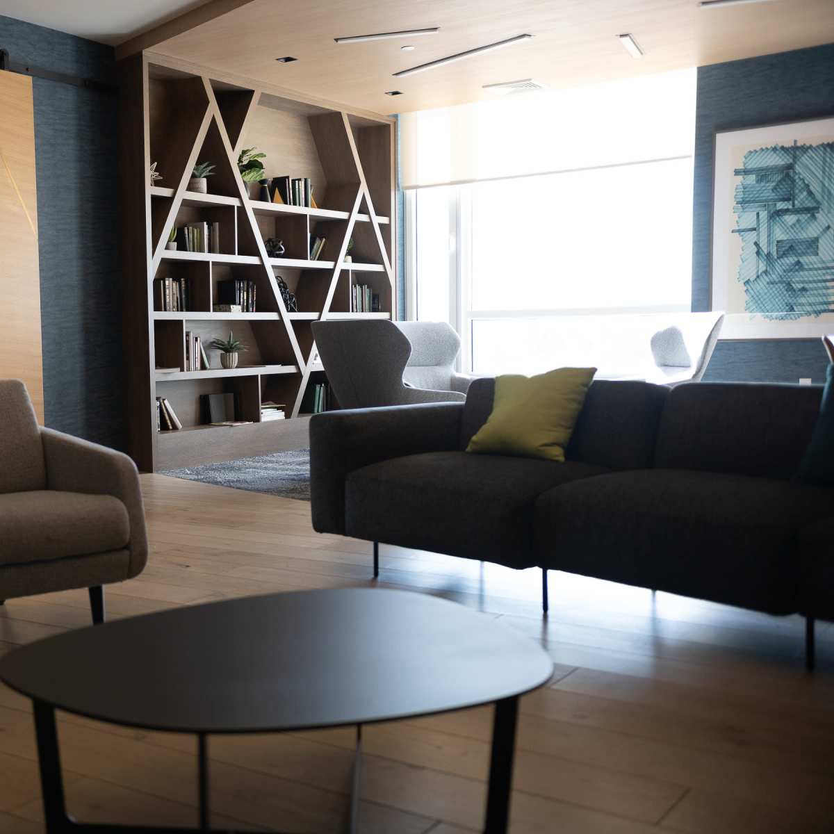 A modern, open-concept lounge area with a coffee table, two armchairs, and a large bookshelf, alongside a view of a dining space in the background.