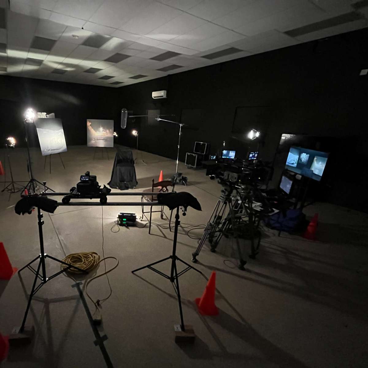 A dimly lit studio setup with cameras, lighting equipment, and orange cones arranged around a central chair and backdrop.
