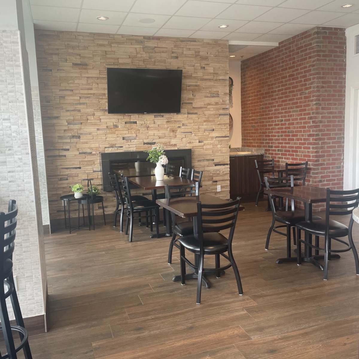 A modern dining area with wooden tables and chairs, a stone feature wall, and a television mounted above a fireplace.