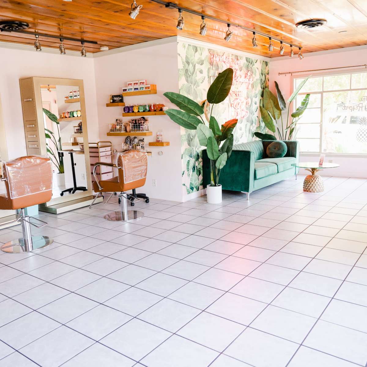 A spacious beauty salon with bright tile flooring, large mirrors, and a green seating area decorated with plants.