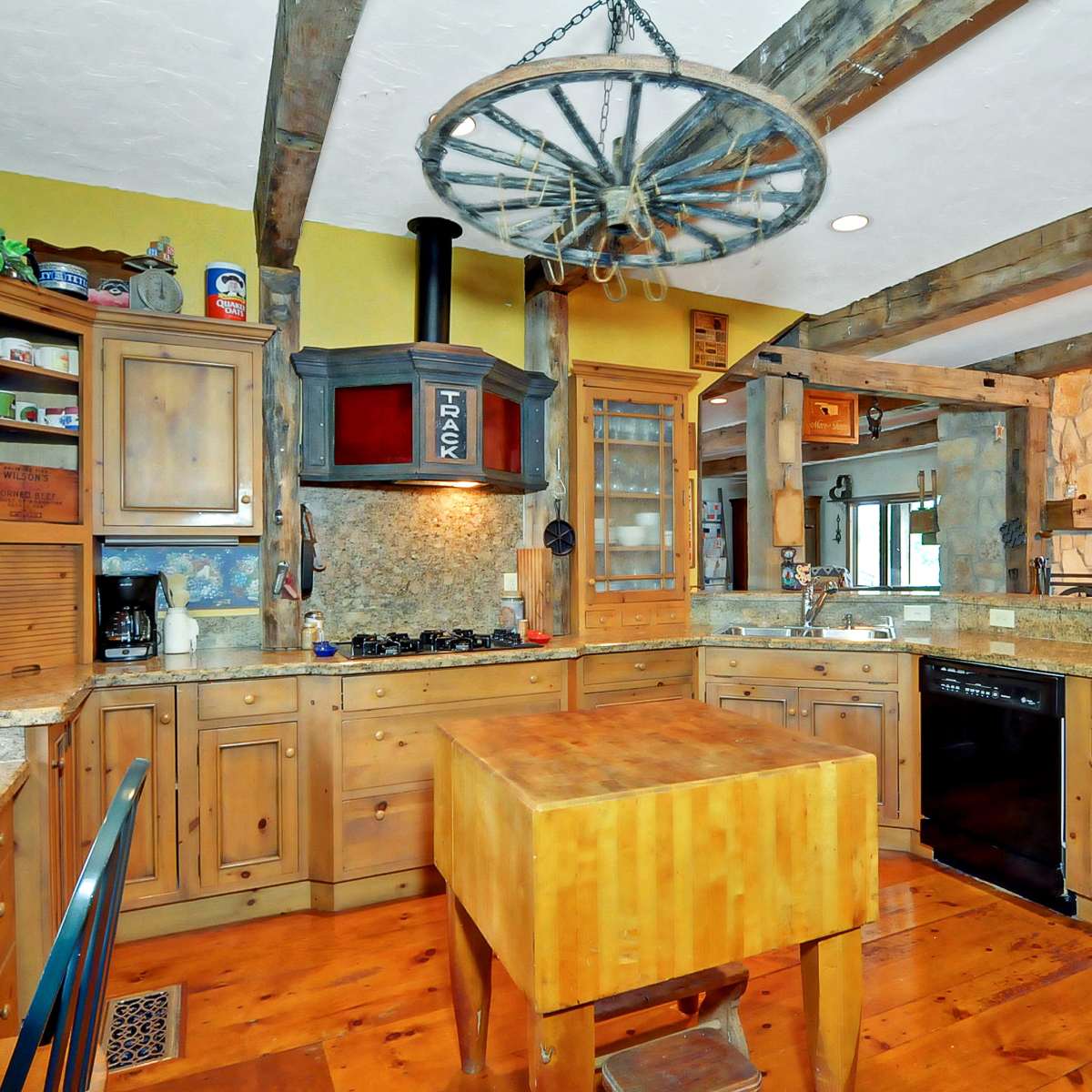 The kitchen features wooden cabinets, a central island made of wood, and a distinct chandelier above, with stone accents and granite countertops.