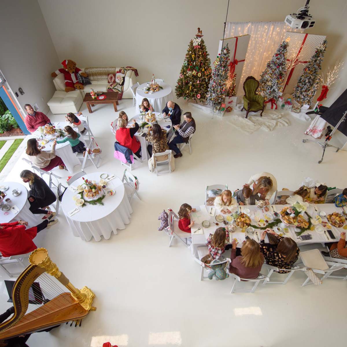 A large gathering of people is seated around tables in a spacious room decorated with Christmas trees and festive decor.