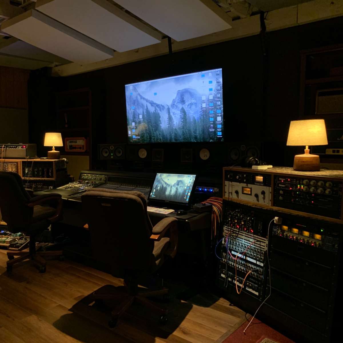 A music recording studio featuring a large screen, mixing console, and various audio equipment in a dimly lit room.