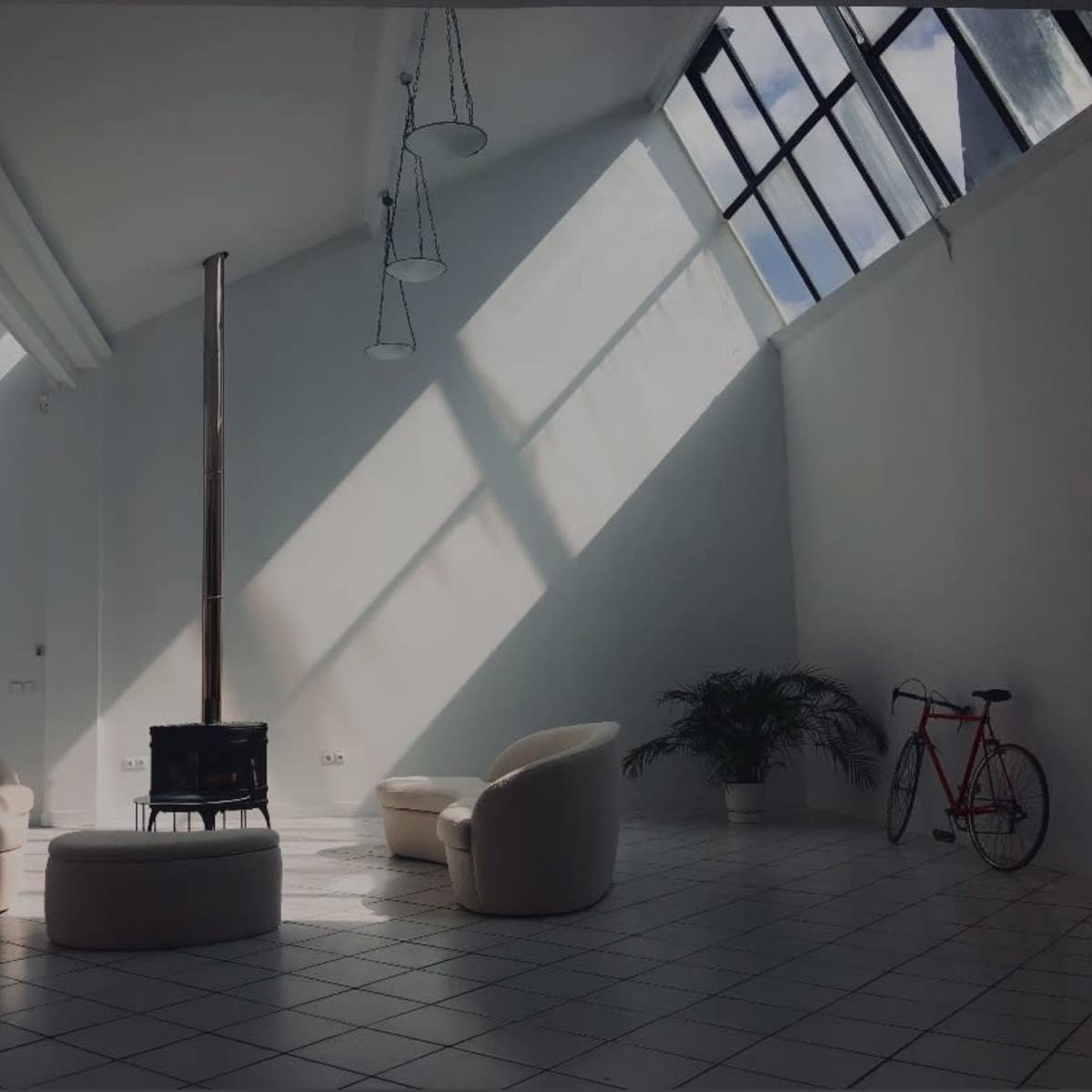 A bright, modern room with two circular chairs, a round table, a wood-burning stove, a potted plant, and a bicycle against a white wall.