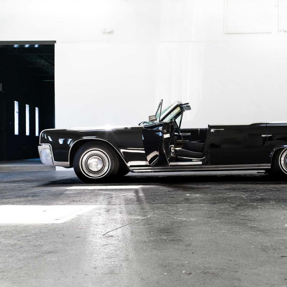 A classic black convertible car parked in an empty industrial space.