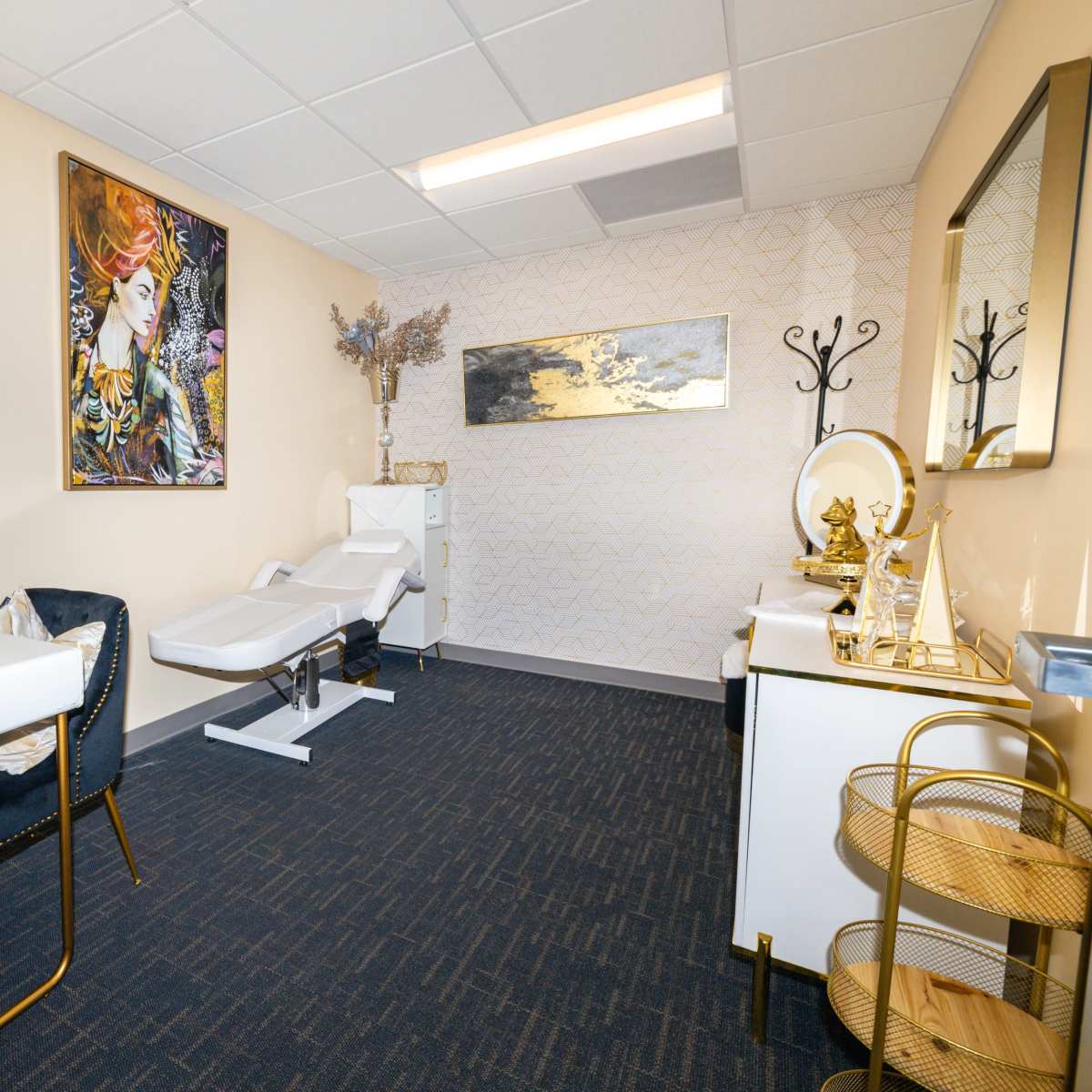 A neatly arranged room featuring two chairs, a treatment bed, a desk, and decorative wall art.