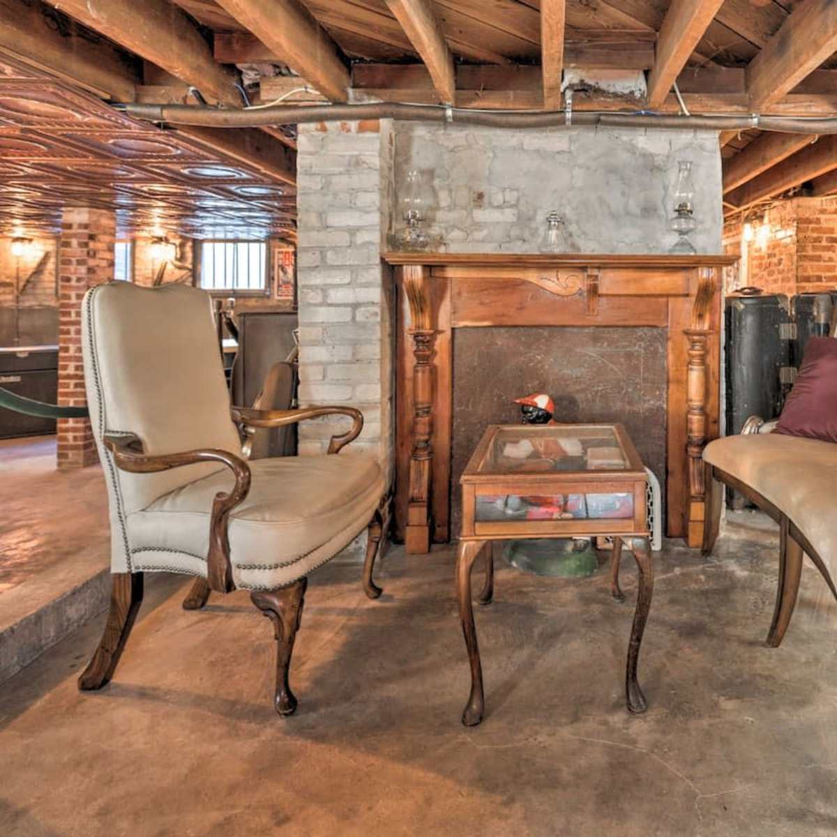 A basement area with two antique-style chairs and a wooden table positioned in front of a brick fireplace.