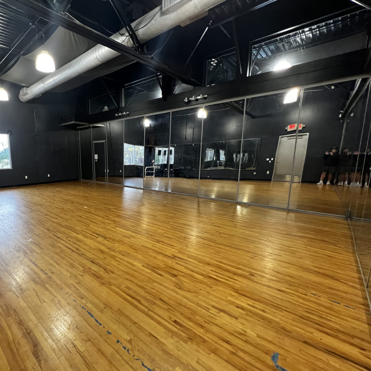 A spacious dance studio with wooden flooring and large mirrors lining one wall.