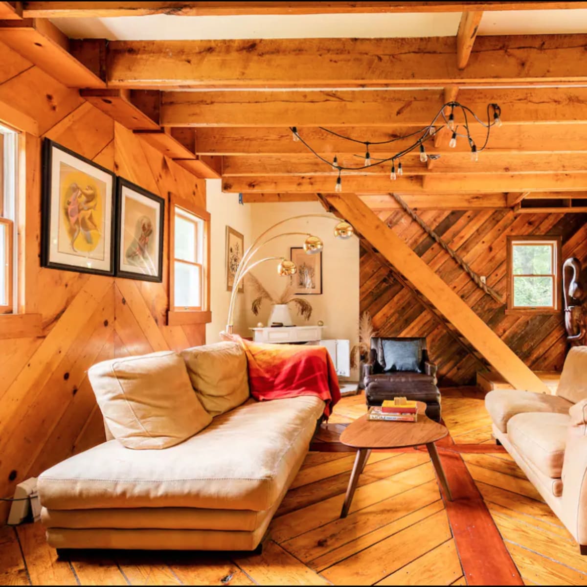 A cozy living room with wooden beams and diagonal wood paneling, featuring two sofas, a circular coffee table, and a staircase.