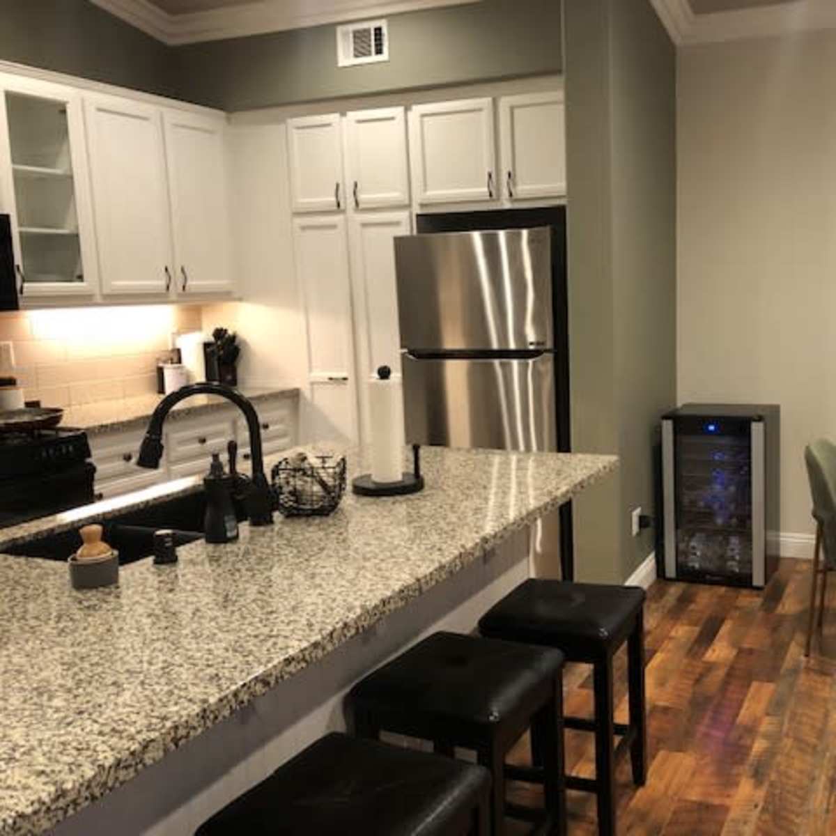 A modern kitchen with white cabinetry, stainless steel appliances, a granite countertop, and a dining table with green chairs.