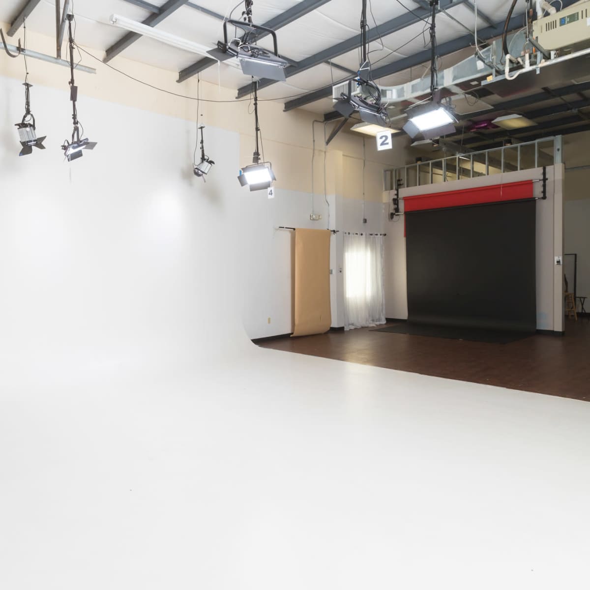 A spacious photography studio featuring a large white backdrop, studio lights, and a dark background setup in the corner.
