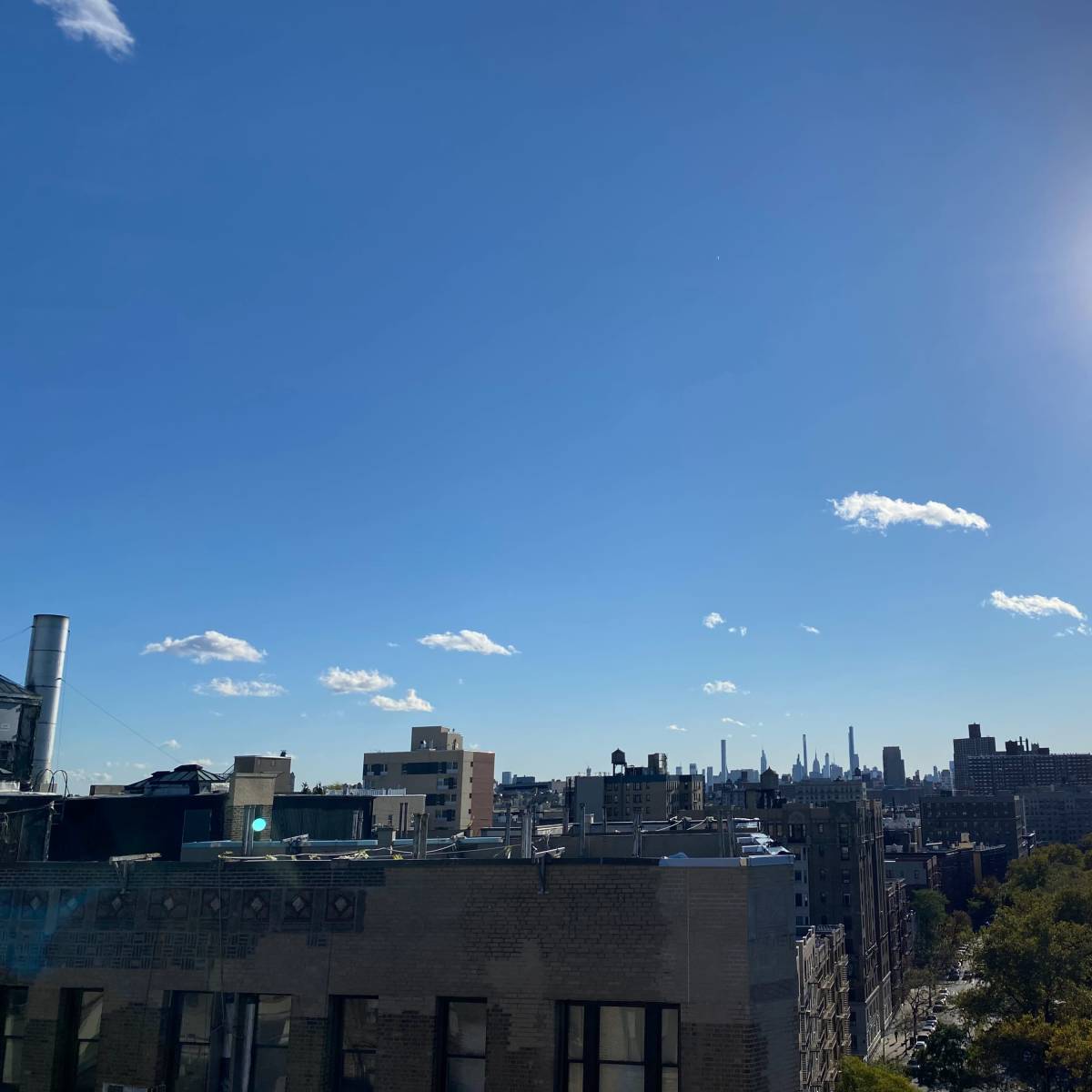 A clear blue sky with a view of a city skyline, including tall buildings, under bright sunlight.