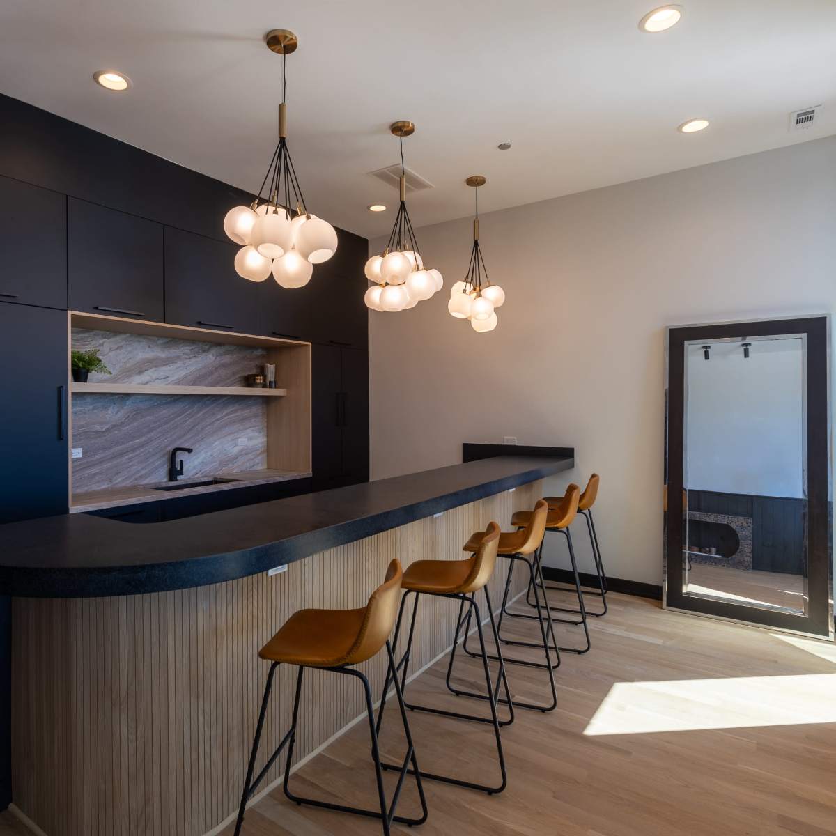 A modern kitchen with a long bar counter, six stools, and stylish pendant lighting.