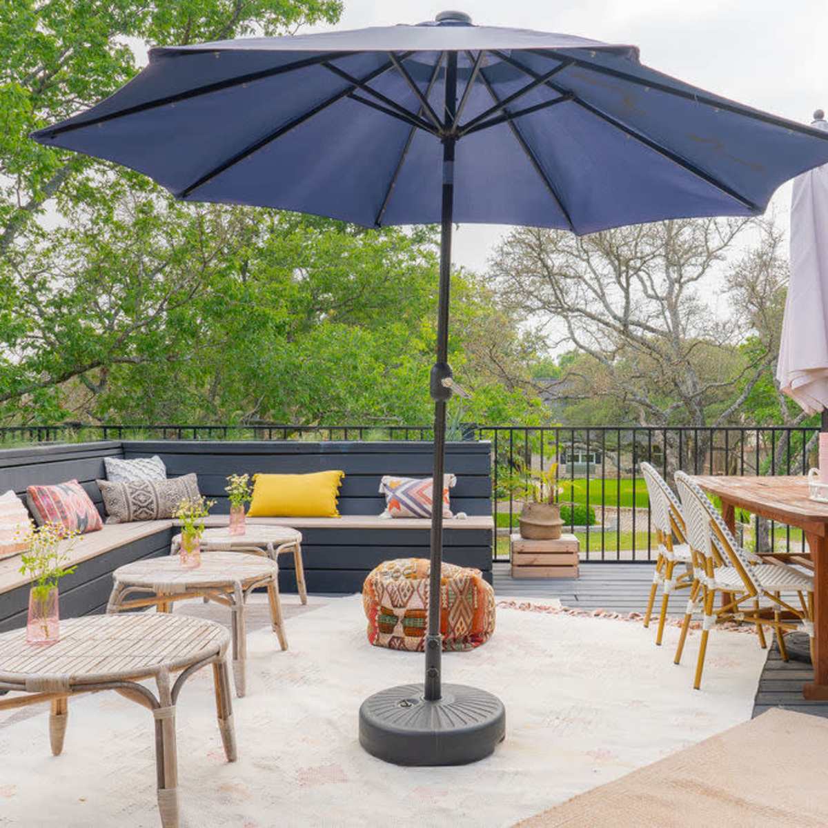 A patio with a seated area featuring a large umbrella, a dining table with chairs, and decorative pillows arranged around a rug.
