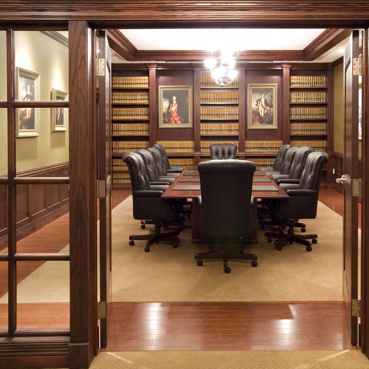 A conference room with a long table and black leather chairs is surrounded by bookshelves filled with books, framed artwork hangs on the walls.