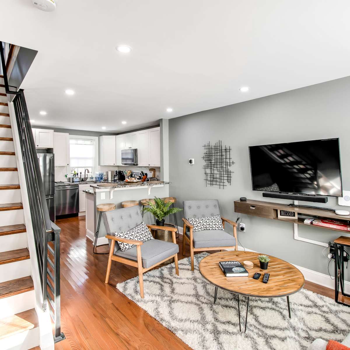 A modern living room with a seating area, a wall-mounted TV, and a staircase leading to an upper level.