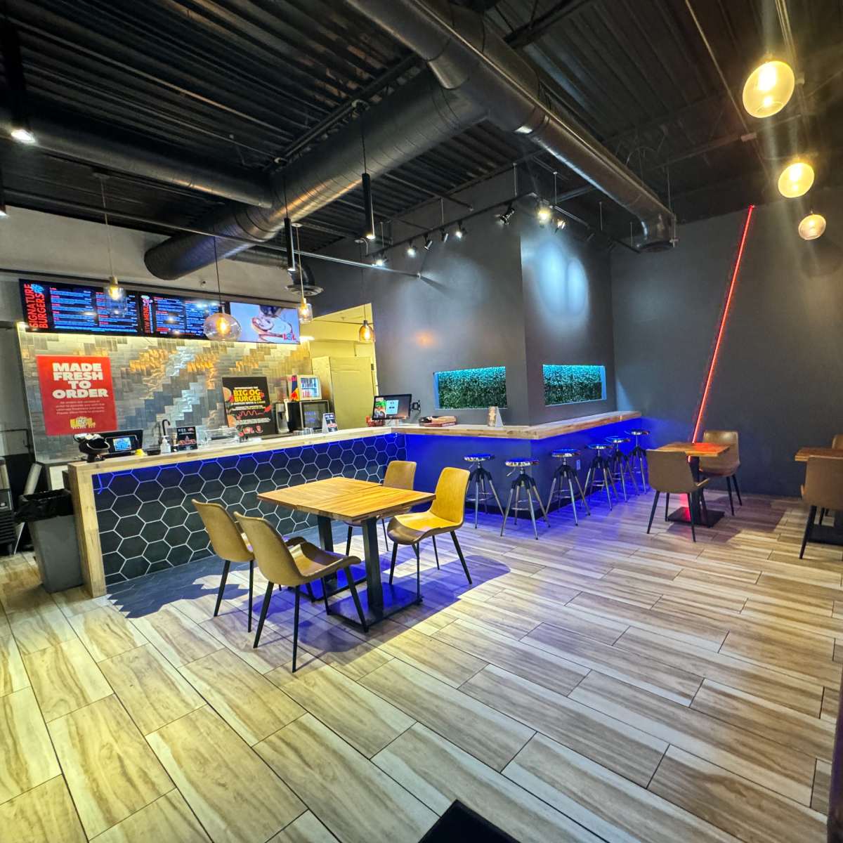 A modern restaurant interior with a counter, seating areas featuring wooden tables and chairs, and decorative lighting.