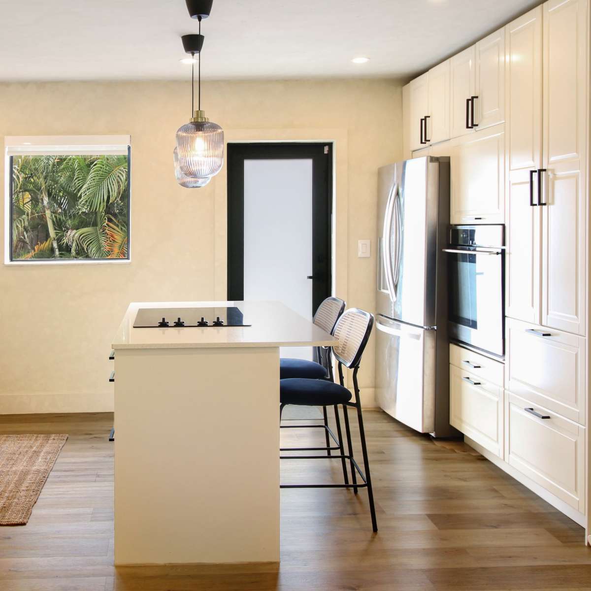 A modern kitchen features white cabinetry, a central island with bar stools, and stainless steel appliances.