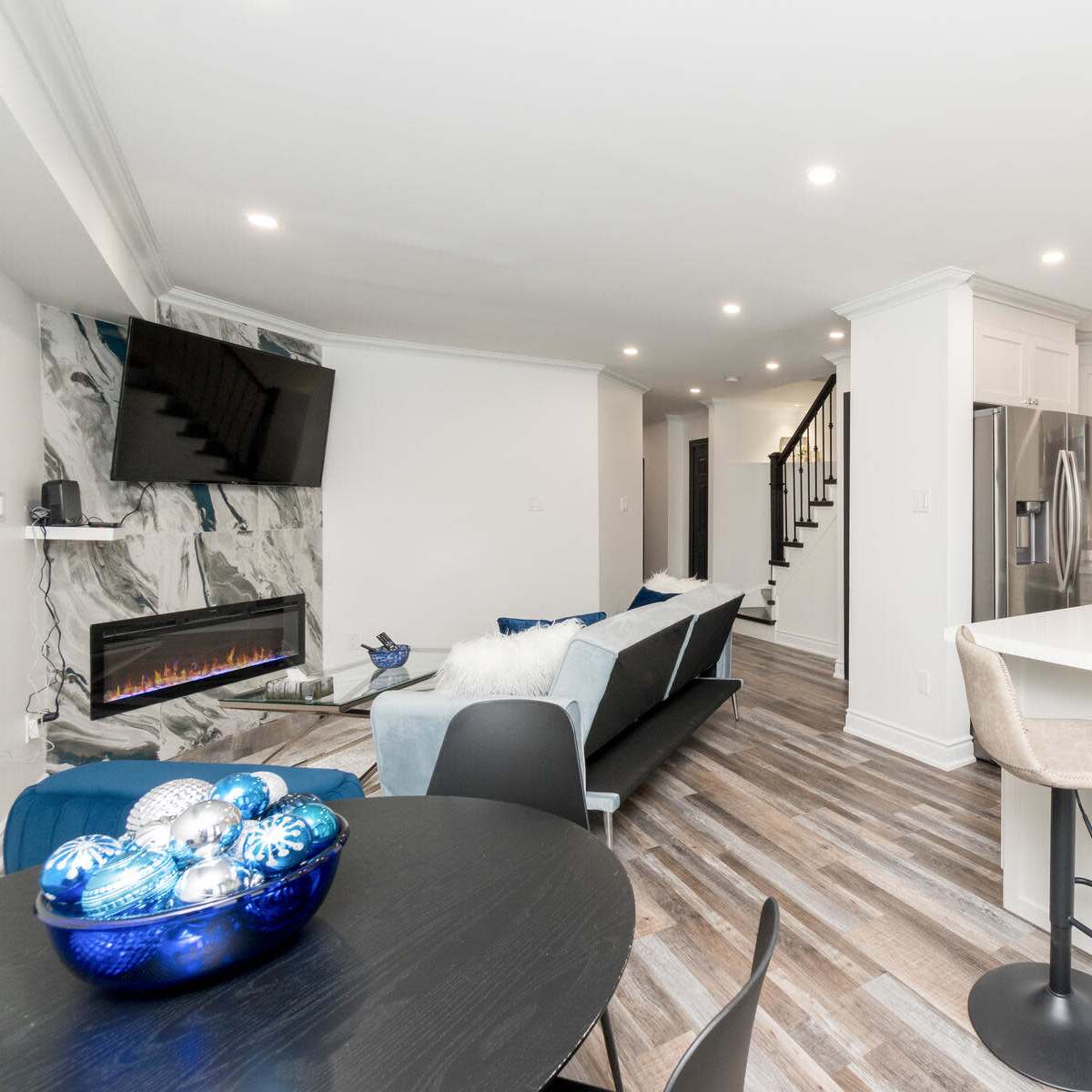 A modern kitchen and living area with a marble accent wall, stainless steel appliances, and a dining table set for four.