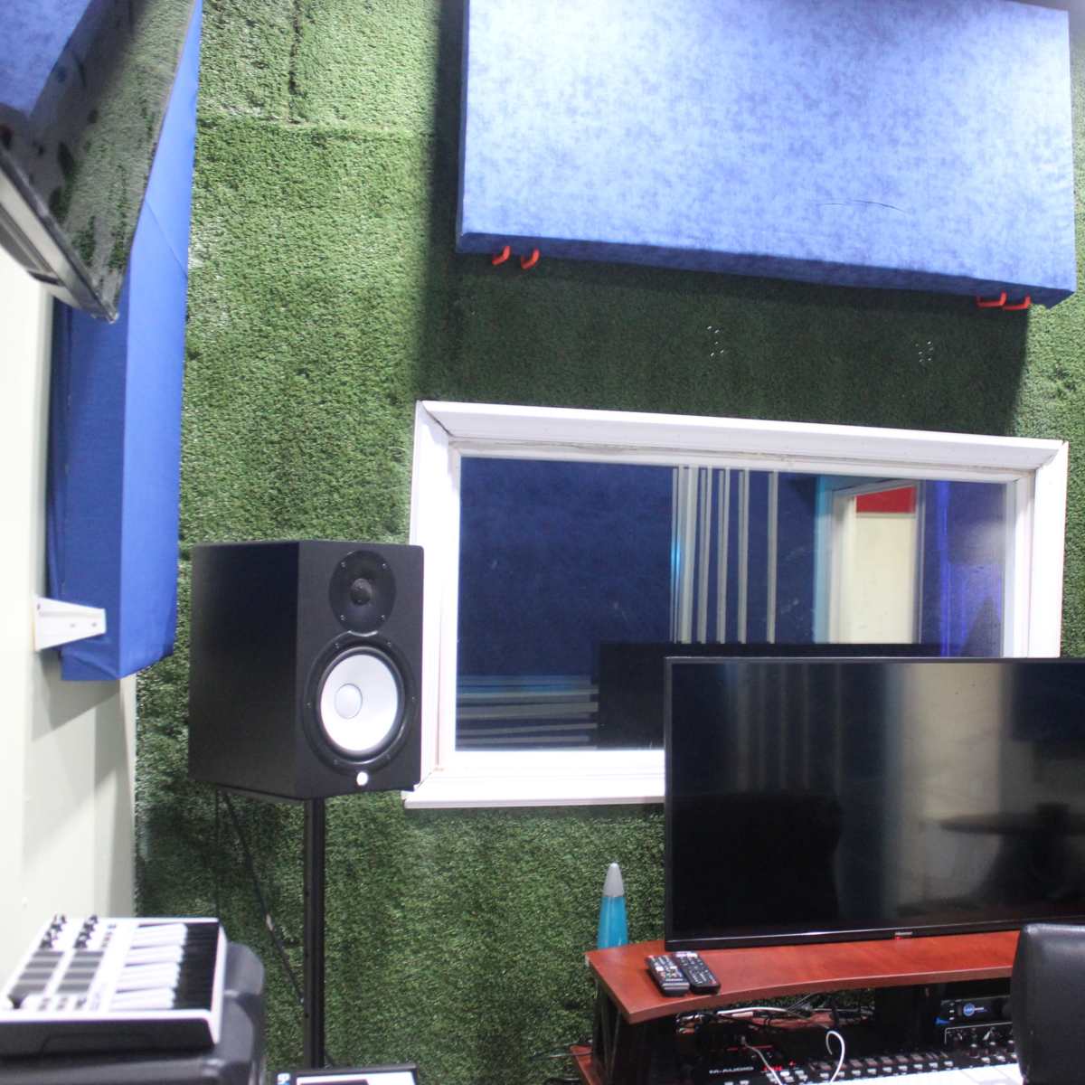 A sound studio with acoustic panels on the walls, a monitor on a desk, and studio speakers on either side of a window.