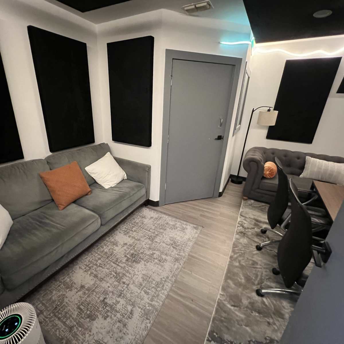 A small, soundproof room with a gray sofa, a chairs, and acoustic panels on the walls.